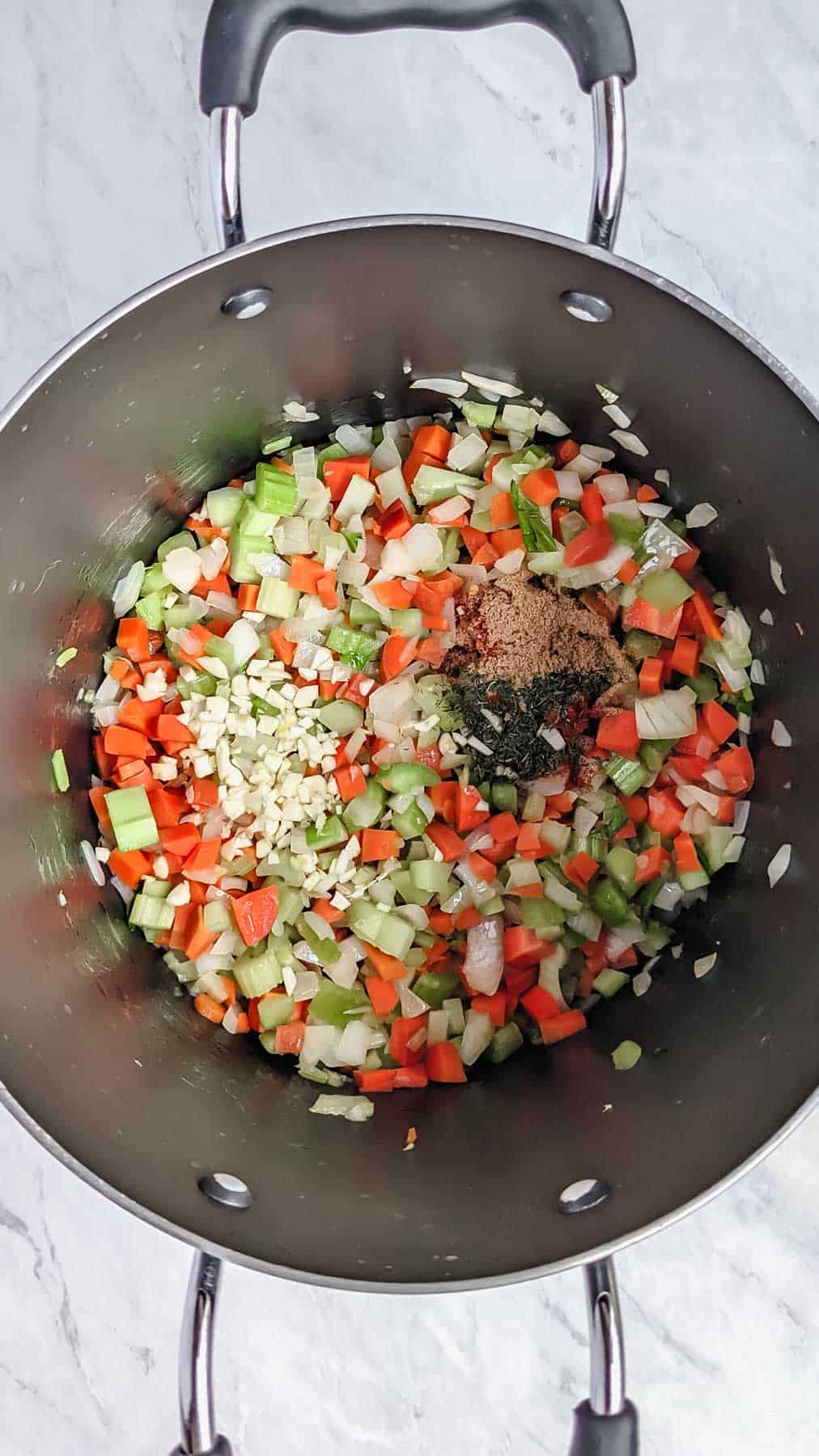Adding in spices and garlic to carrots, onions, celery mixture in large soup pot