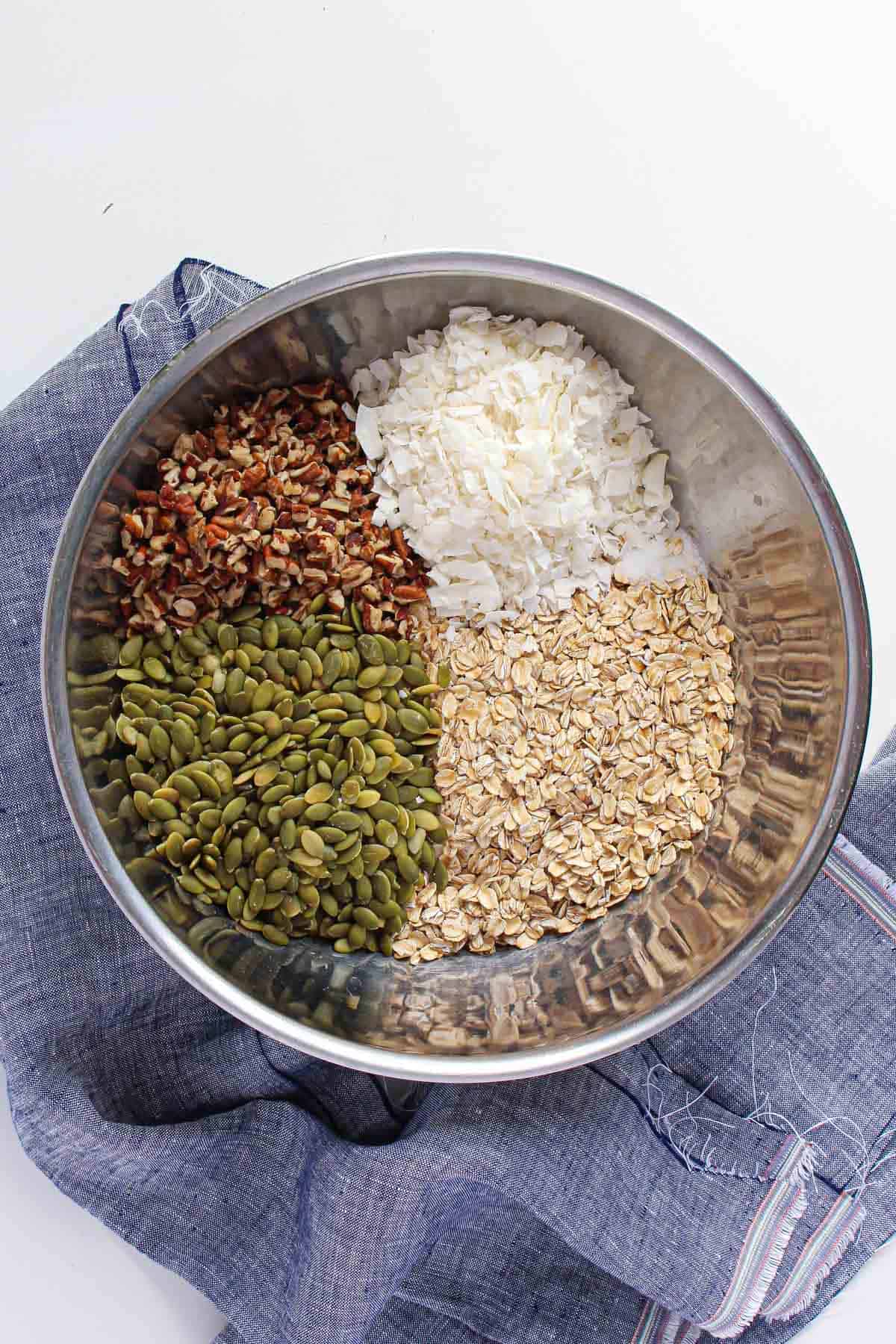 Stainless steel mixing bowl with pepitas, shredded coconut, oats, and pecan pieces