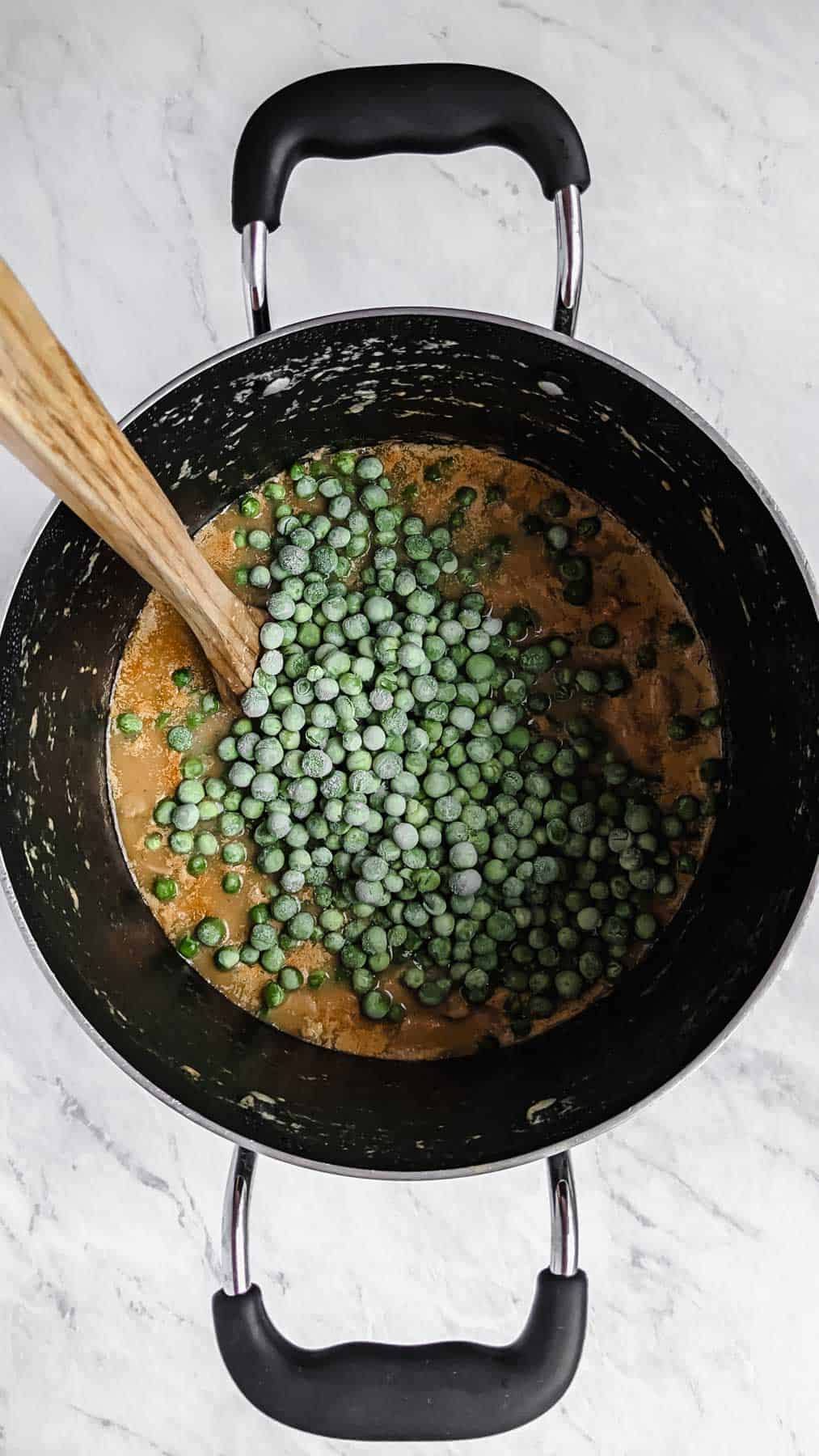 Frozen peas added into soup pot on top of other ingredients already in the soup.