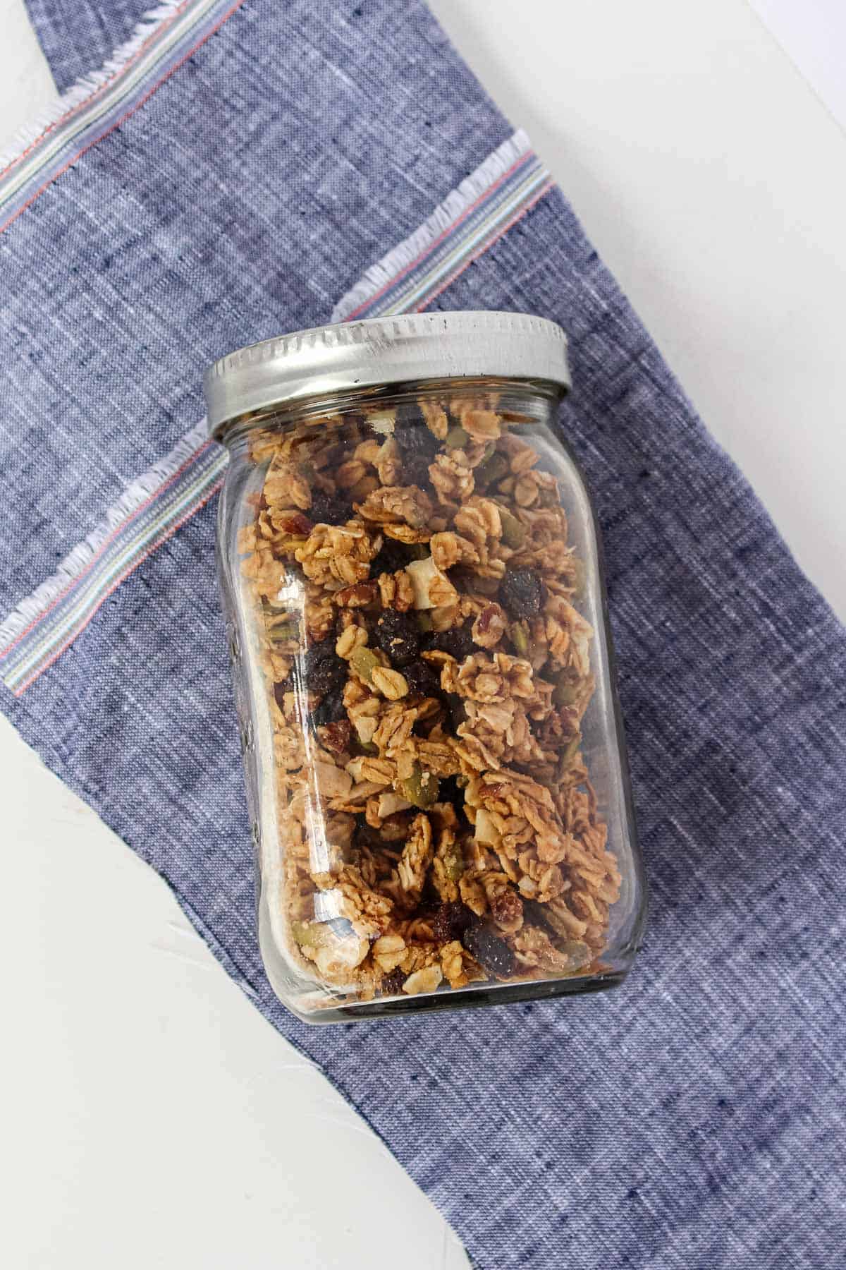 Homemade peanut butter granola in a mason jar laying on its side on top of a blue napkin.
