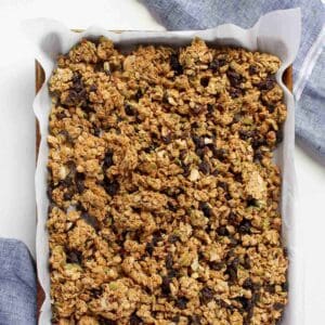 Homemade peanut butter granola on baking sheet lined with white parchment paper with two blue napkins in the background.