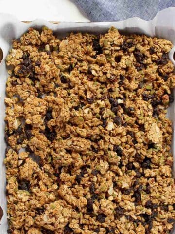 Homemade peanut butter granola on baking sheet lined with white parchment paper with two blue napkins in the background.