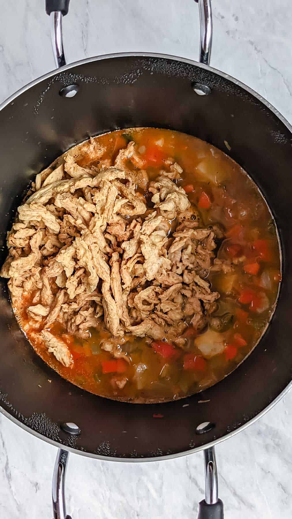 Dried soy curls added on top of other ingredients already in soup pot. Marble background.