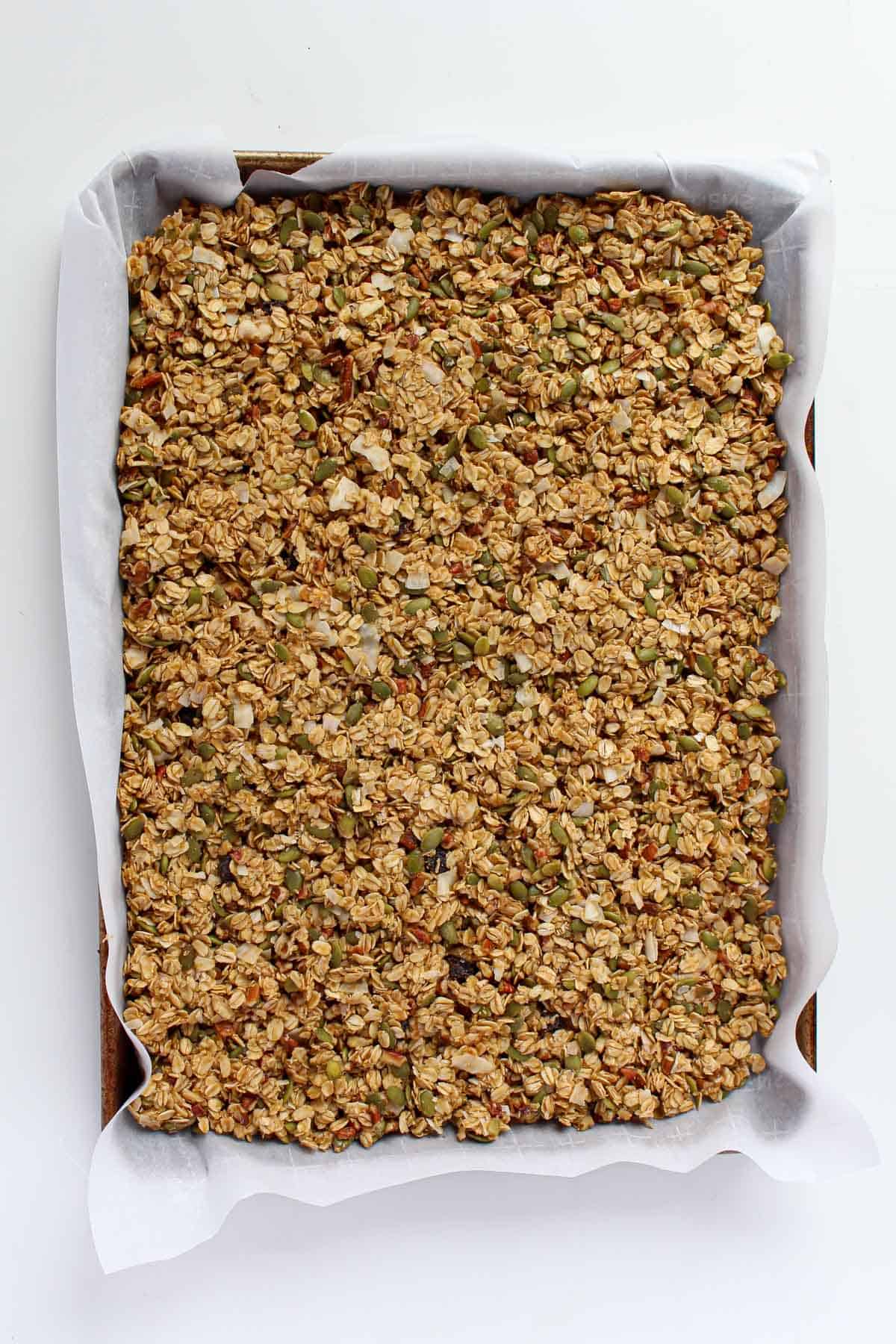 Uncooked granola on a baking sheet lined with white parchment paper.