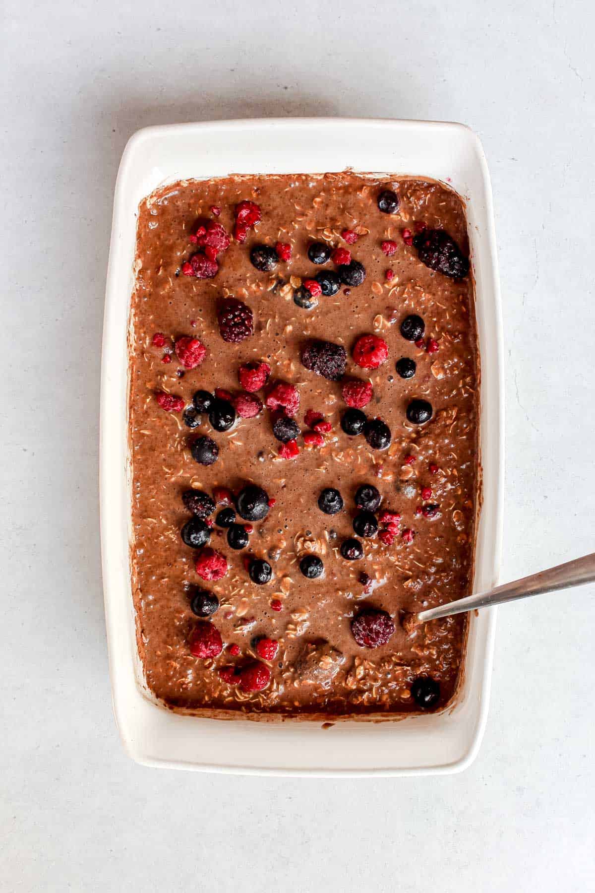 Chocolate banana baked oatmeal with mixed frozen berries in a white baking dish, uncooked and ready to go in the oven.