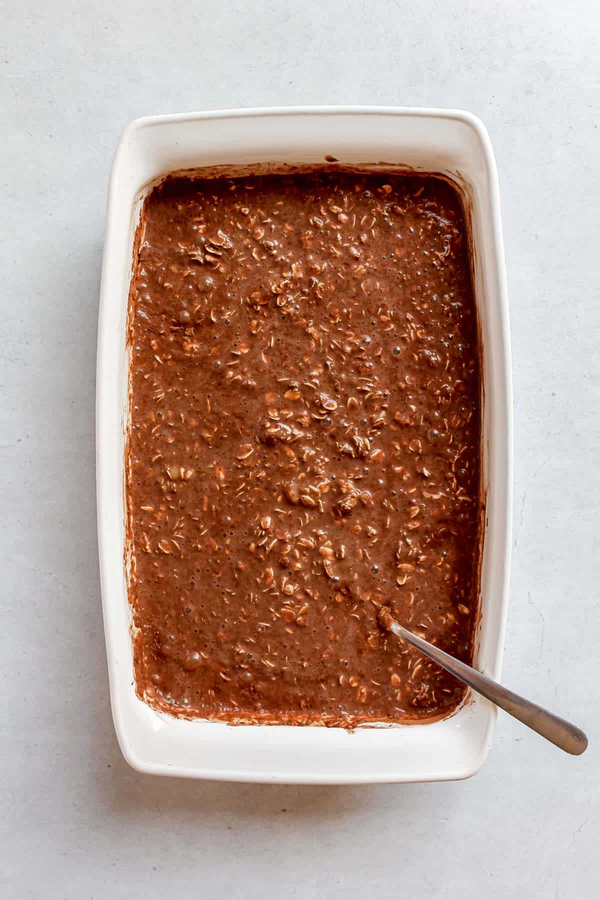Cocoa powder mixed into the oatmeal bake in a white baking dish.