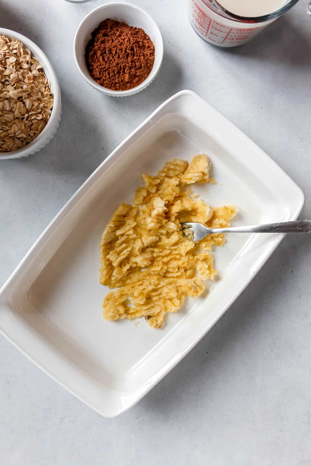 Smashed banana in white baking dish with a fork.