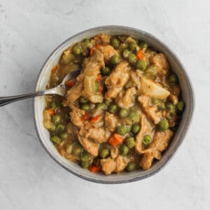 Vegan soup with soy curls, potatoes, green peas, and carrots in a grey bowl and silver spoon on. a marble background