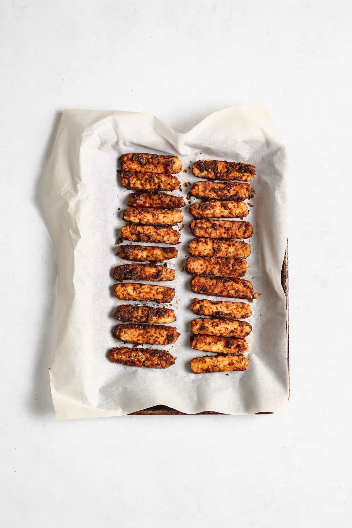 Baked tempeh on parchment paper on top of a baking sheet.