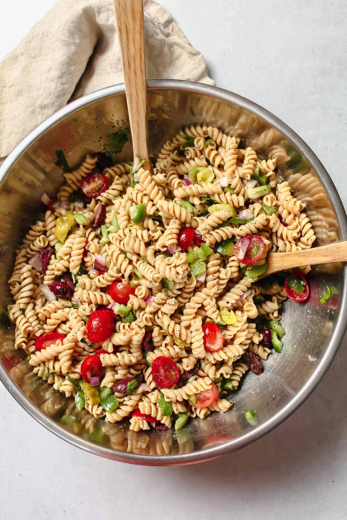 Pasta salad ingredients in large mixing bowl with two wooden spoons