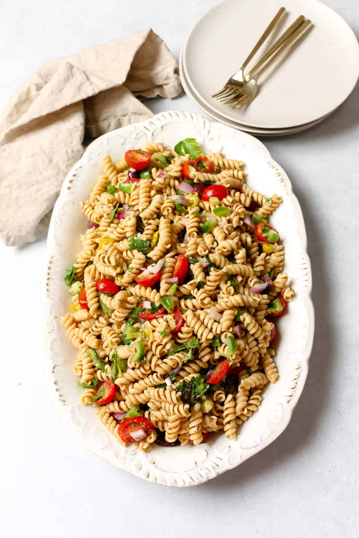 Easy vegan pasta salad presented in a white serving dish with two plates and forks on the side.