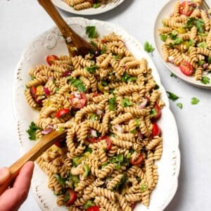 Easy vegan pasta salad on white serving platter being served with two wooden serving spoons