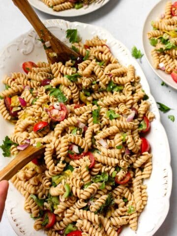 Easy vegan pasta salad on white serving platter being served with two wooden serving spoons
