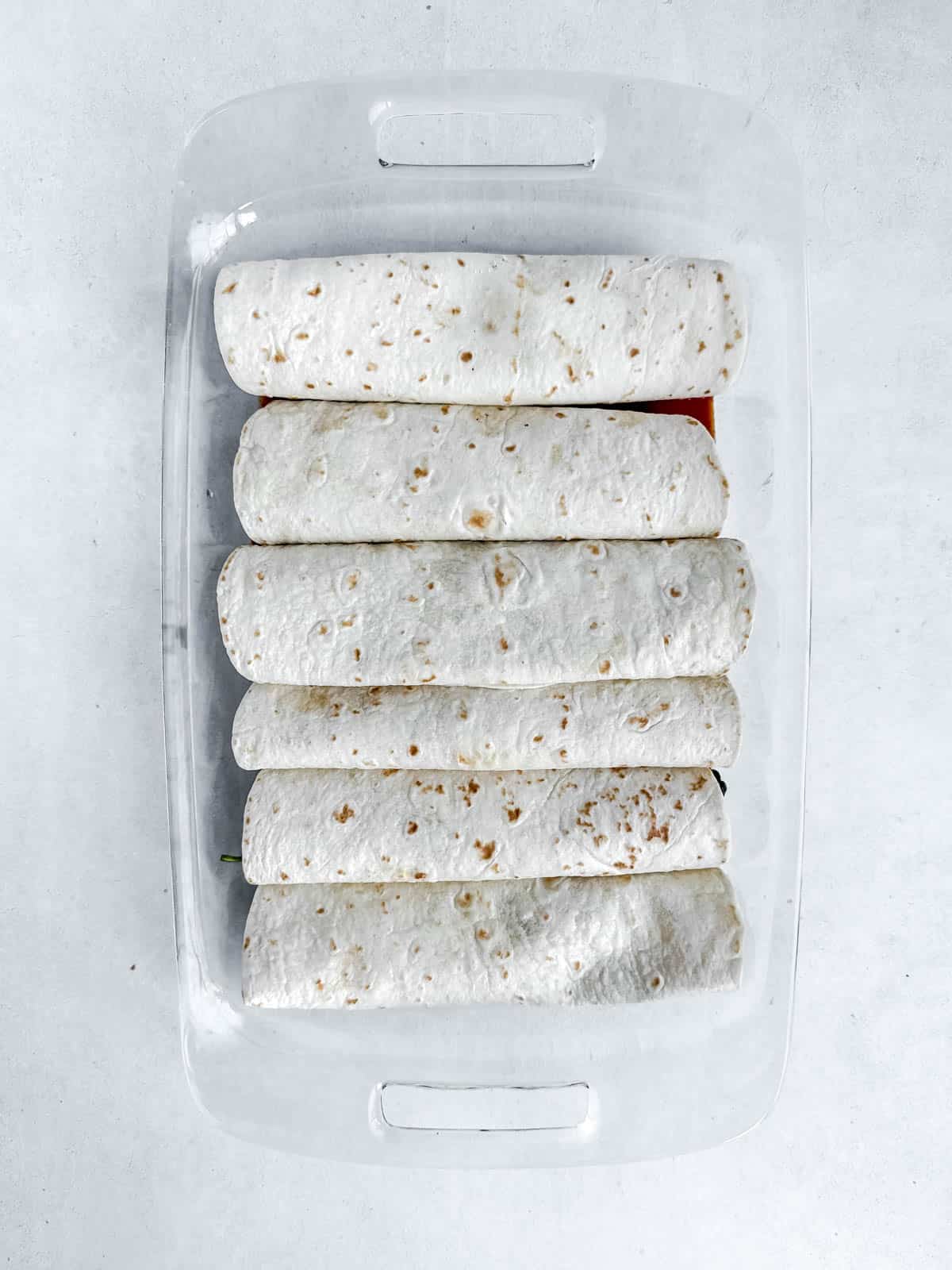 Baking dish full of wrapped enchiladas on white background