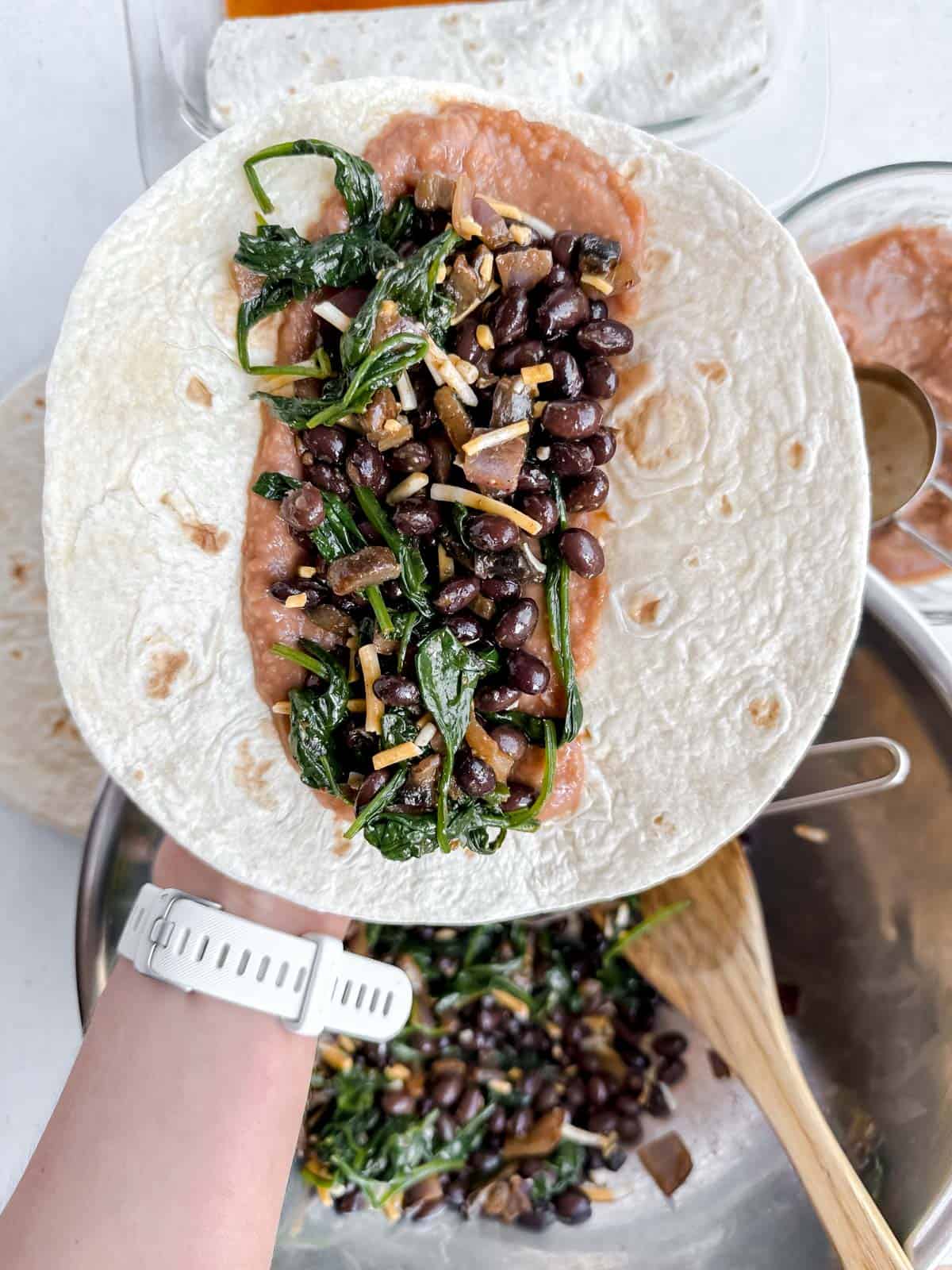 Black bean and vegetable mixture placed on top of refried beans down the center of a flour tortilla.