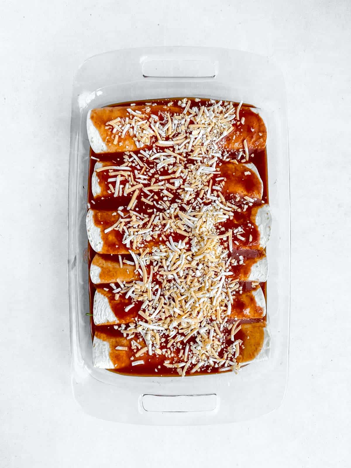Pre-cooked Enchiladas with sauce and cheese on top in glass baking dish