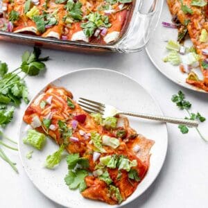 Vegan Black Bean Spinach Enchilada topped with lettuce, red onion, and cilantro served on white plate with a fork.