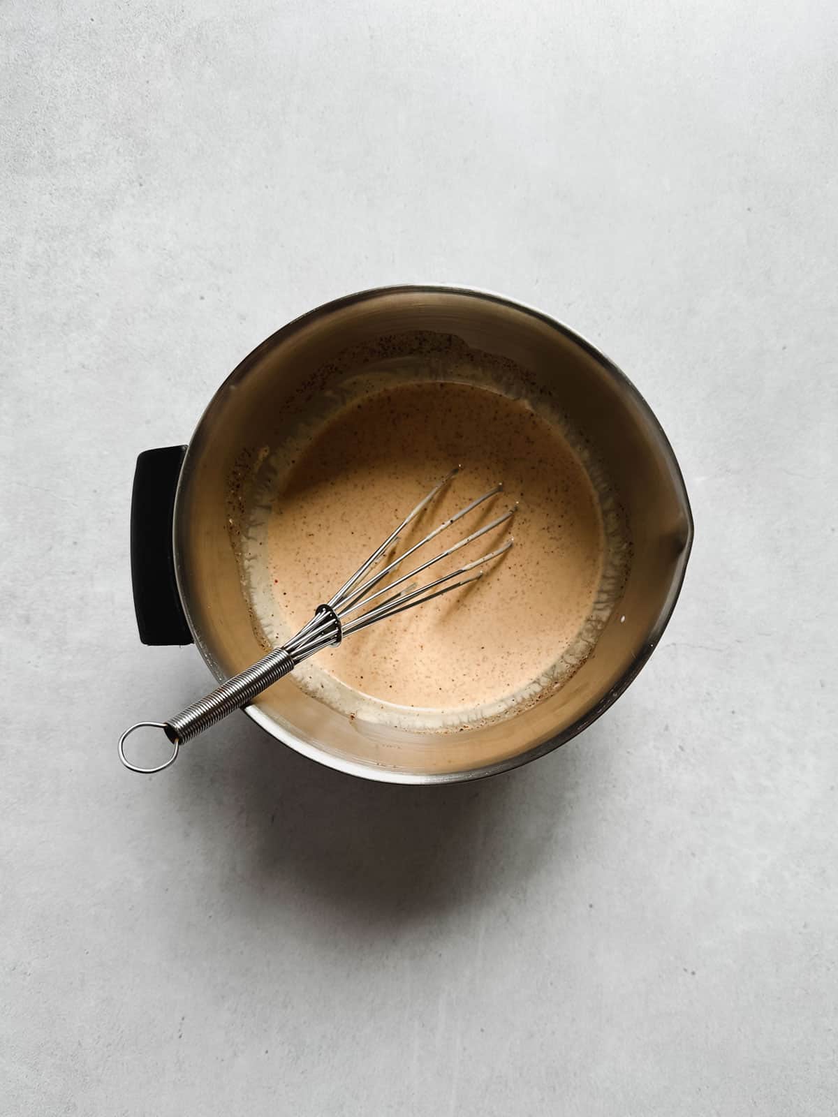 Stainless steel mixing bowl filled with dressing and a whisk.