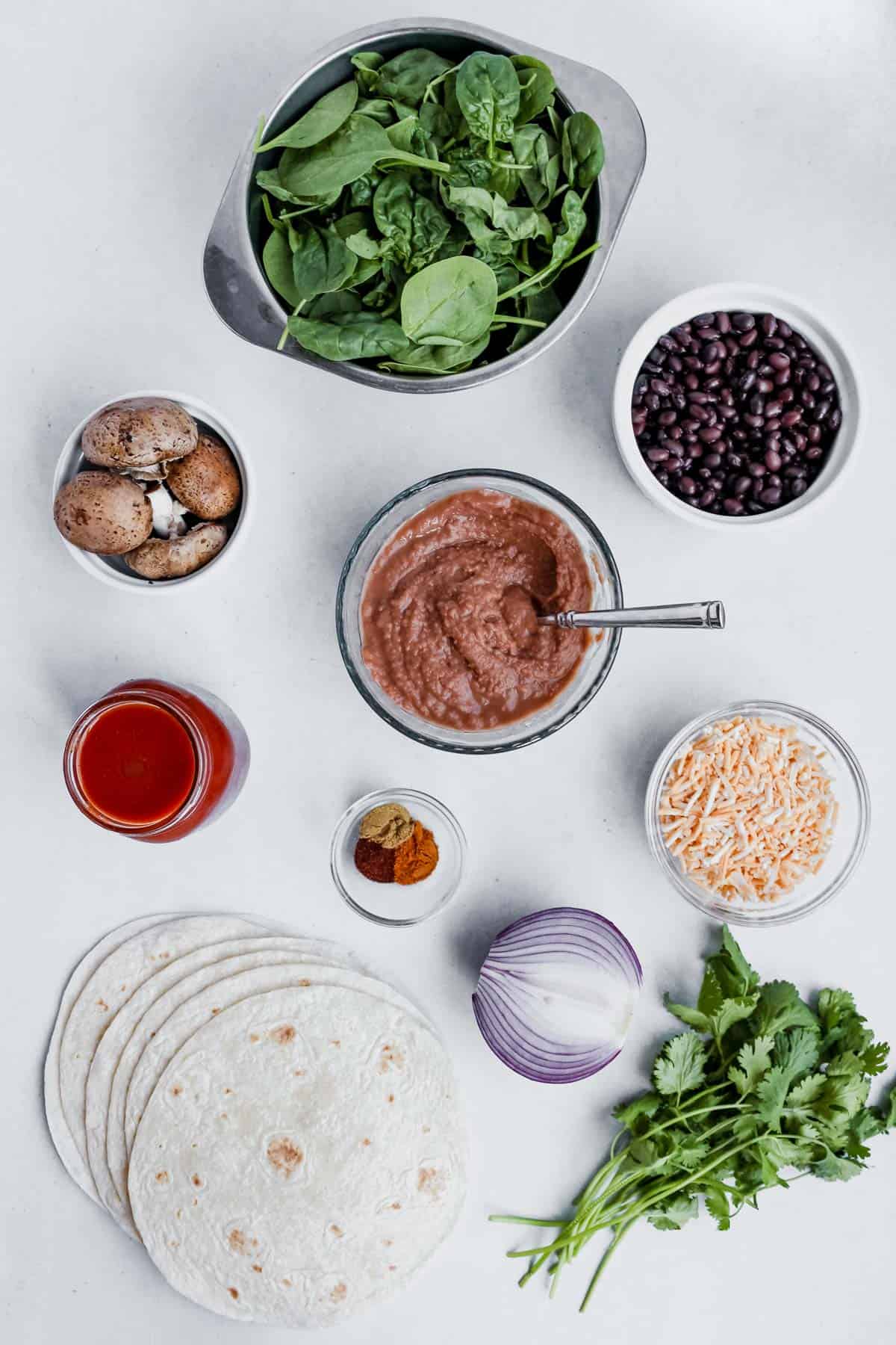 Individual enchilada ingredients placed in bowls or sitting on white background