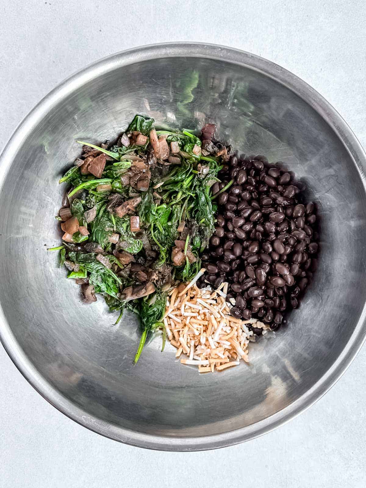 Black beans, sautéed vegetables, and plant-based cheese in stainless steel mixing bowl