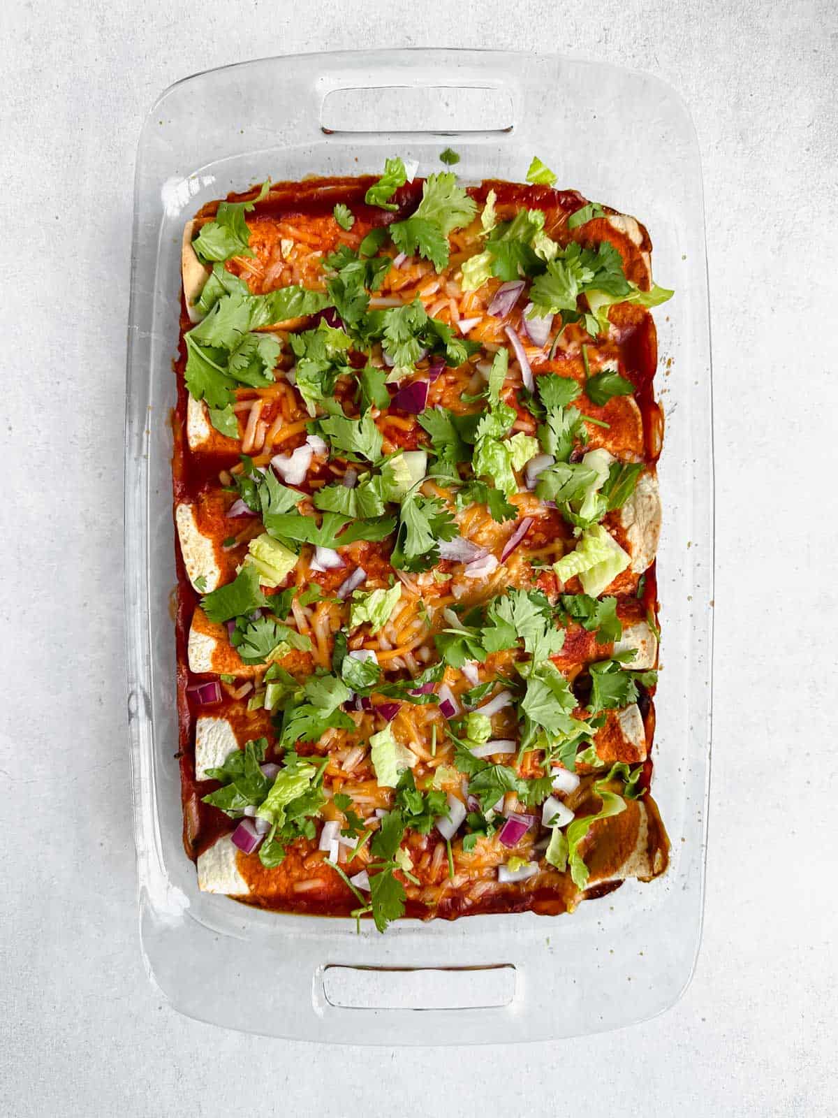 Baked vegan black bean spinach enchiladas topped with lettuce, cilantro and red onion