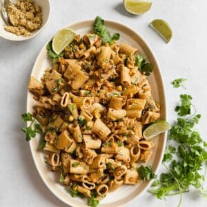 Vegan street corn pasta salad served on oval dish garnished with fresh cilantro, limes, and vegan cotija cheese.