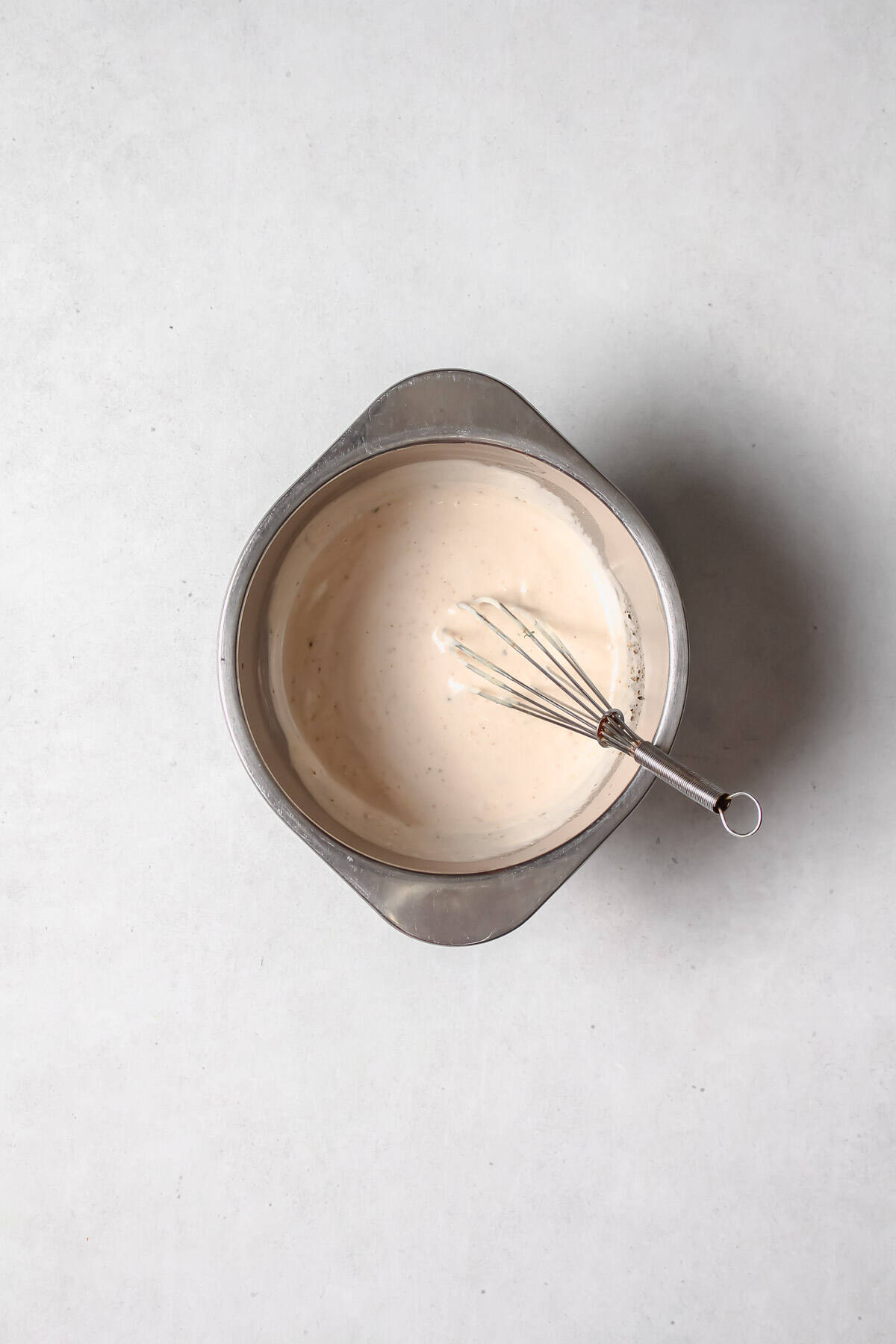 Creamy vegan salad dressing in stainless steel bowl with whisk.