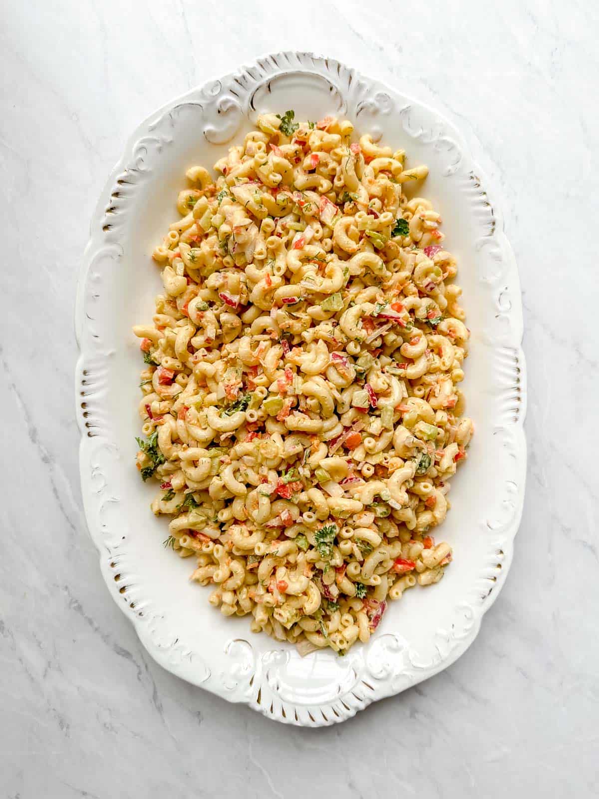 Creamy vegan macaroni salad in white serving platter on a marble background