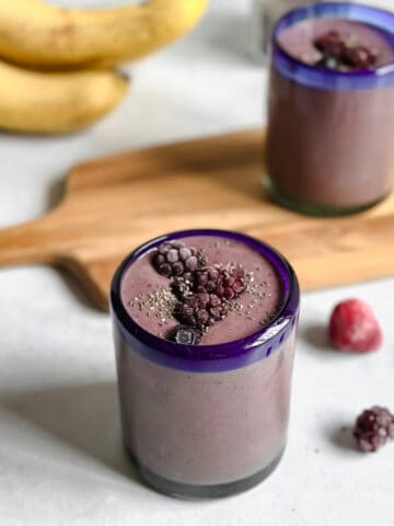 Two glasses filled with a berry smoothie garnished with frozen berries and chia seeds.
