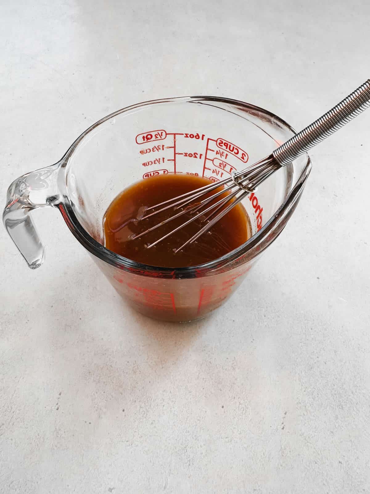 Better Than Bouillon mixed with water in a glass measuring jar with a small whisk.