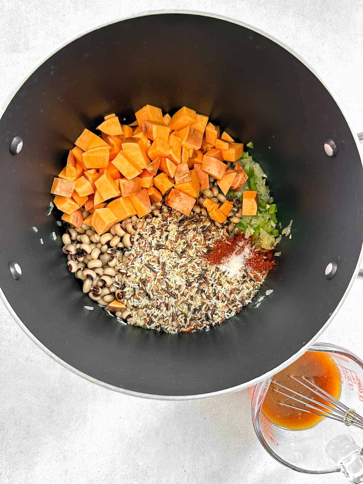 Black-eyed peas, green bell pepper, rice, liquid smoke and spices in soup pot with bouillon off to the side