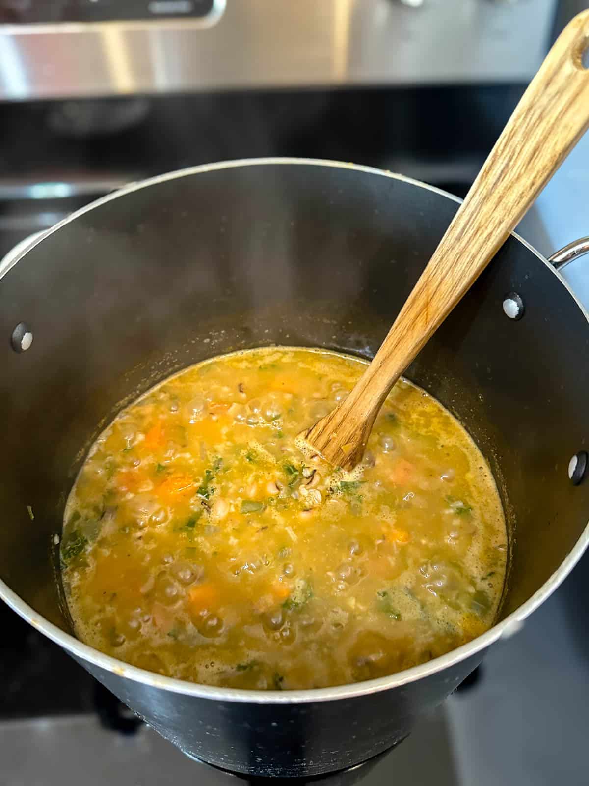 Cooking black-eyed pea soup recipe with rice, sweet potato and kale on the stove top.