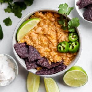 A bowl of vegan white chicken chili topped with a slice of lime, jalapeños, and blue tortilla chips