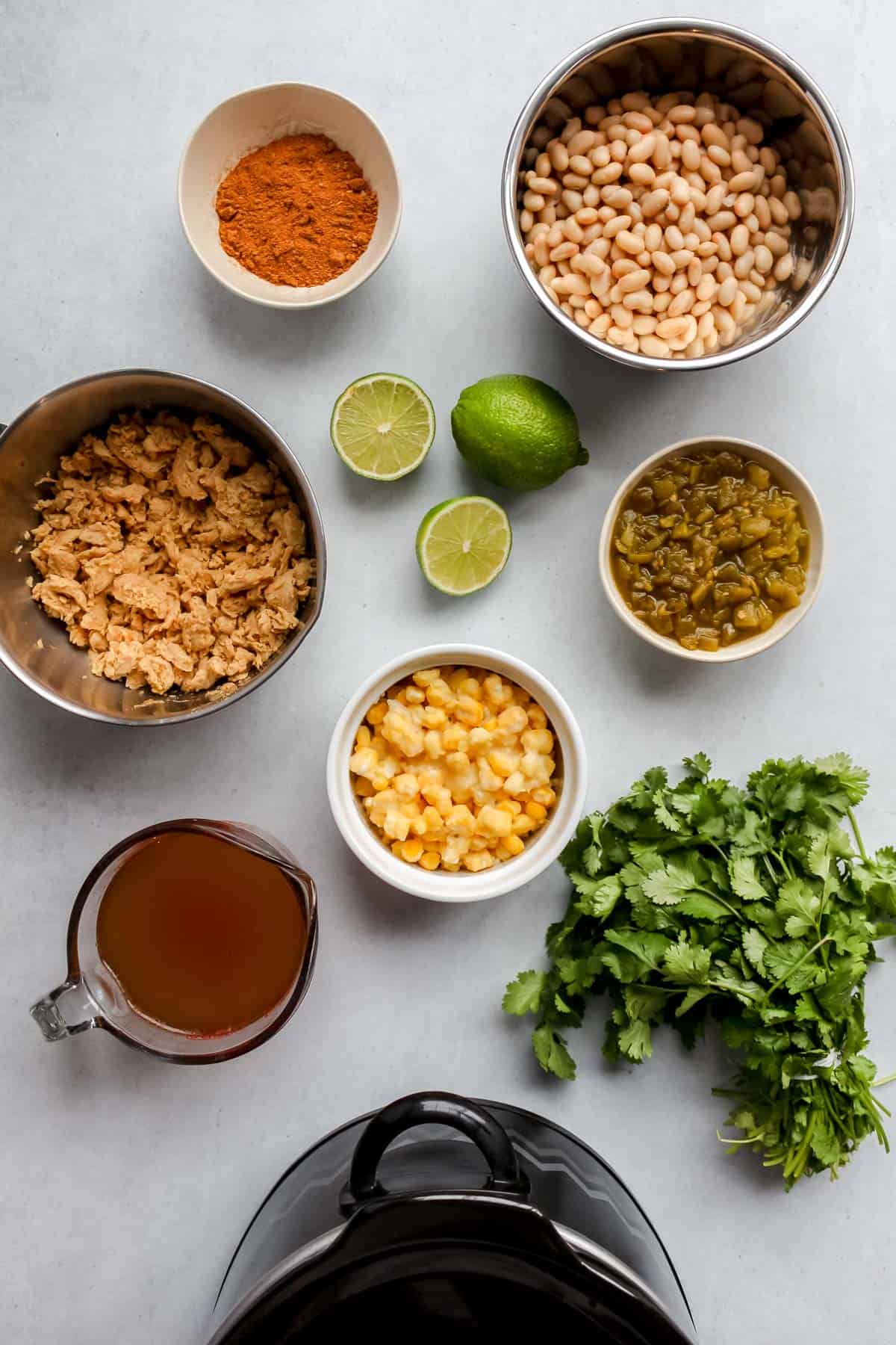 Individual ingredients in bowls or containers on a grey background and part of a slow cooker in view at the bottom of the image.
