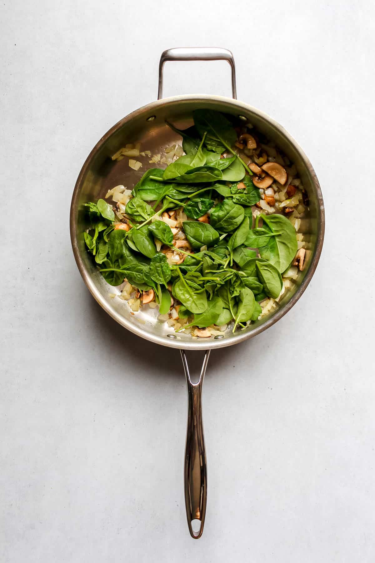 Sautéed onions, mushrooms and spinach in stainless steel skillet on white background