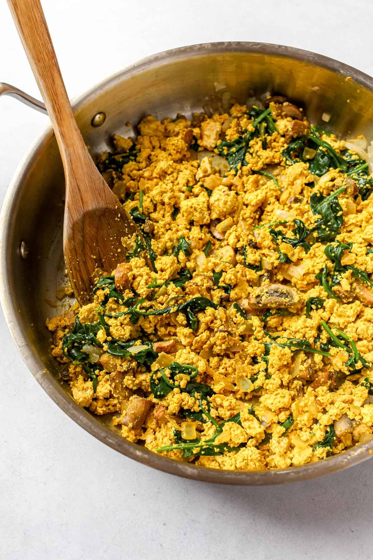 Tofu scramble in stainless steel skillet with wooden spoon