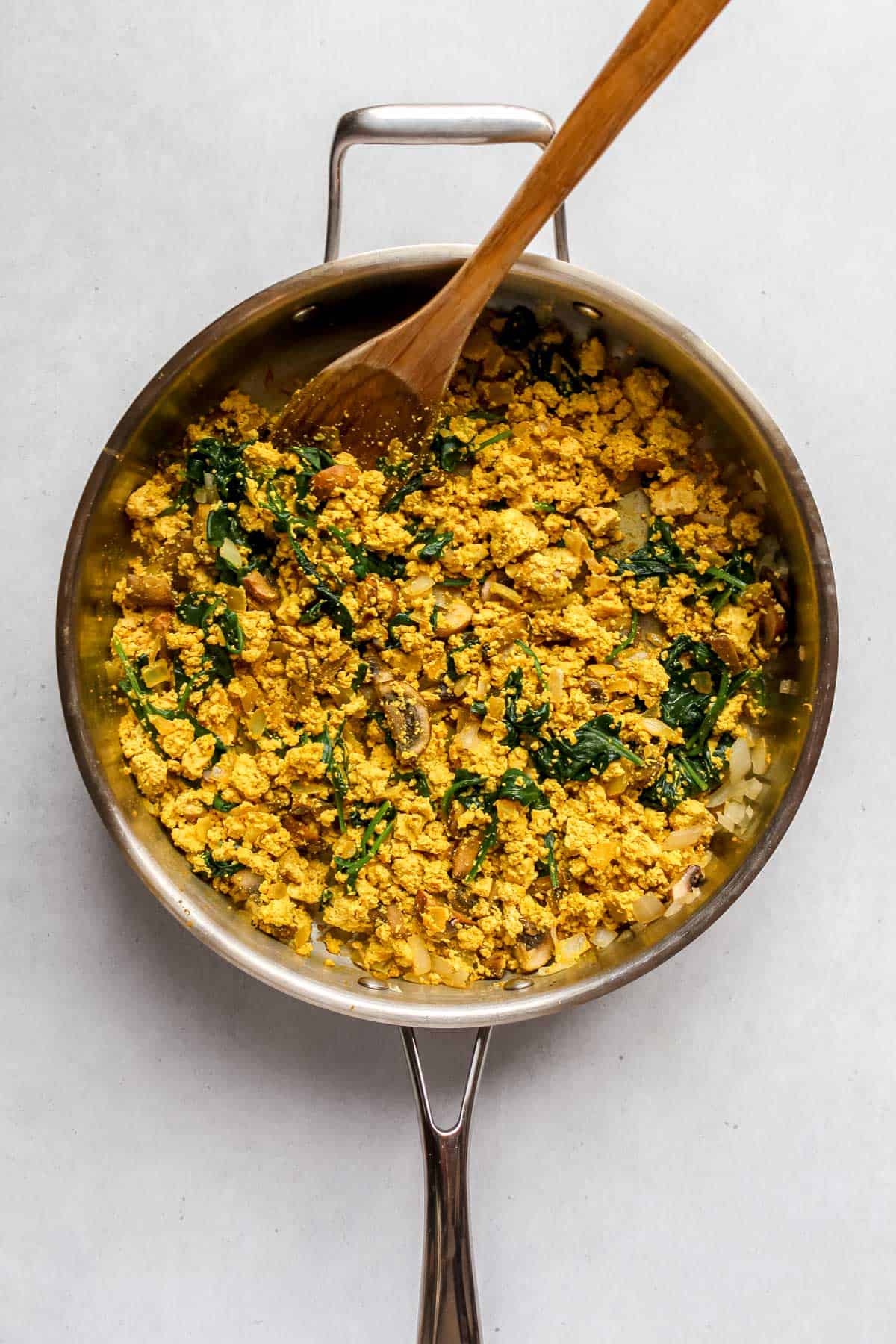Tofu scramble with sautéed vegetables in skillet with wooden spoon