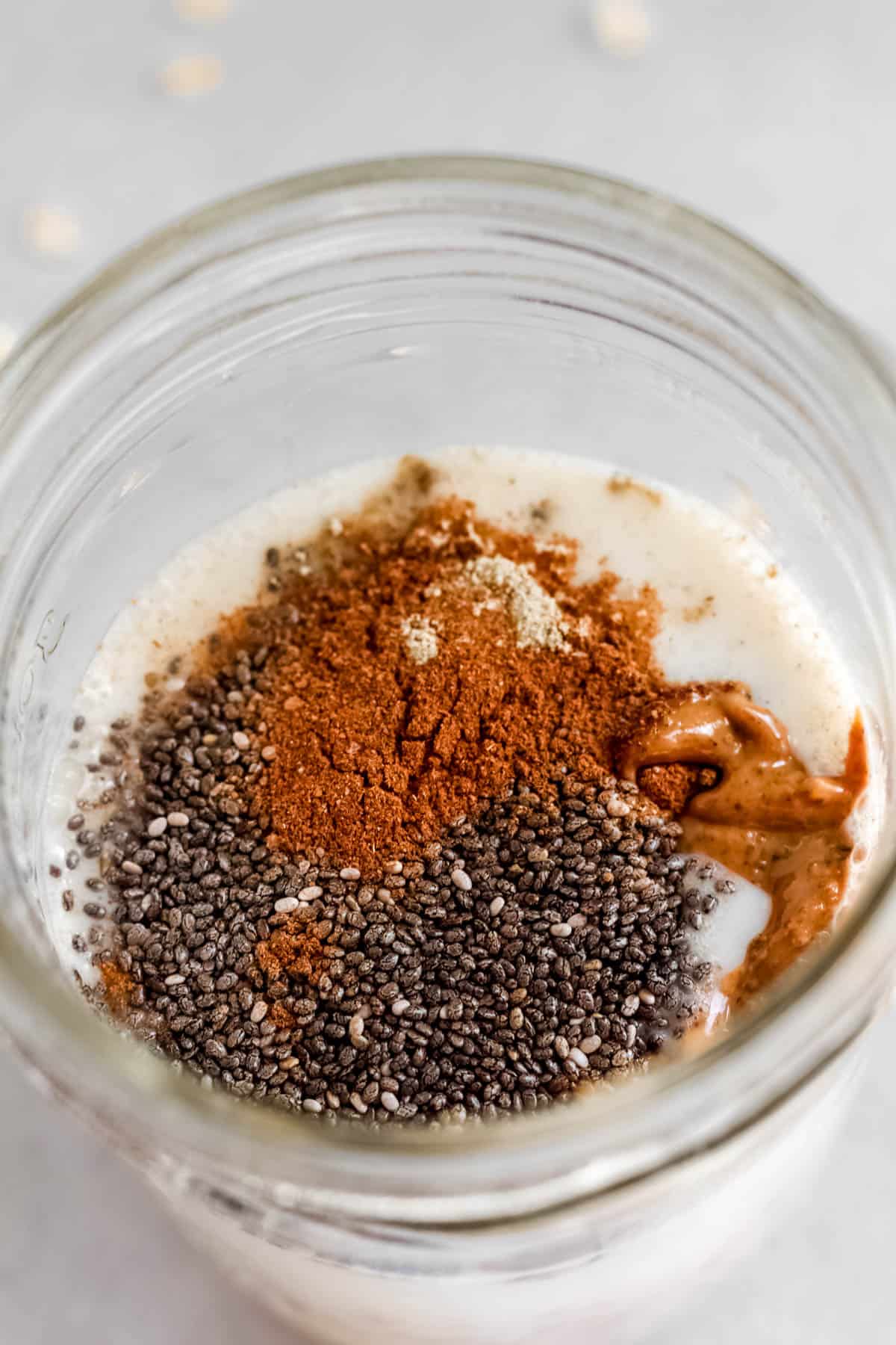 Oats, spices, almond milk, chia seeds and nut butter in mason jar