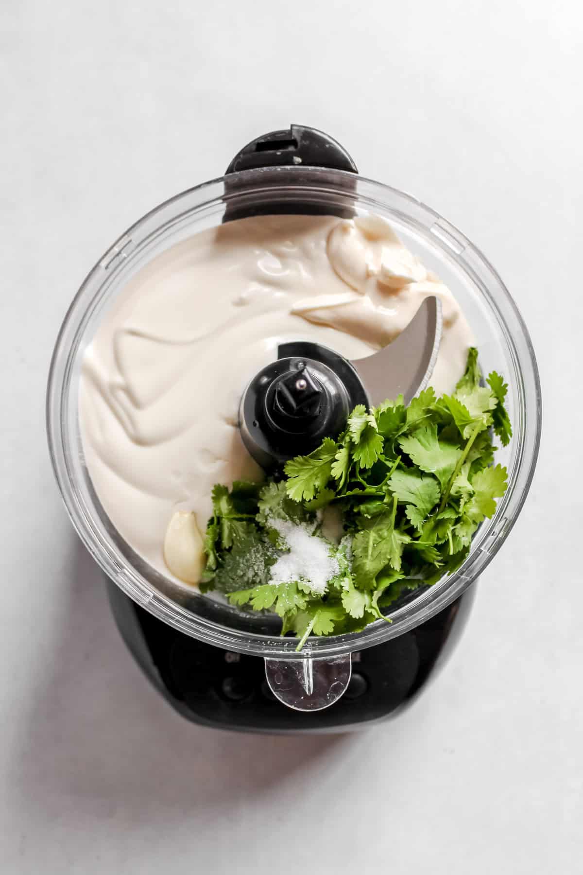 All vegan crema ingredients in a black food processor on a white background.