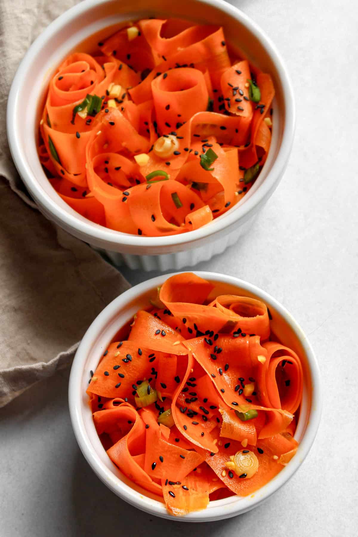 Two white bowls filled with carrot salad topped with sesame seeds and green onions.