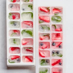 Blueberries, strawberries and mint frozen in white ice cube trays