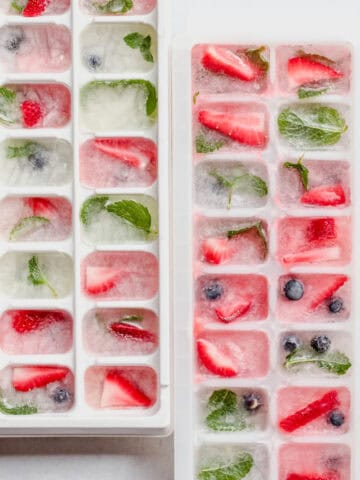 Blueberries, strawberries and mint frozen in white ice cube trays