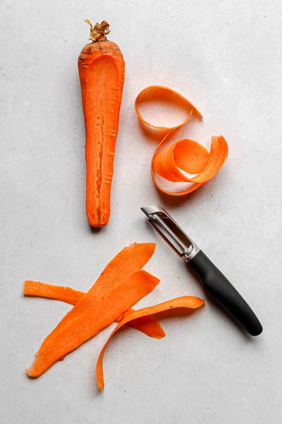 1 large carrot along with a vegetable peeler and several strips, or ribbons, of carrot.