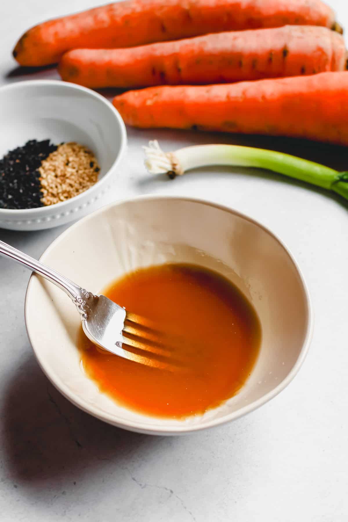 Sesame ginger dressing in small white bowl with a fork for whisking.