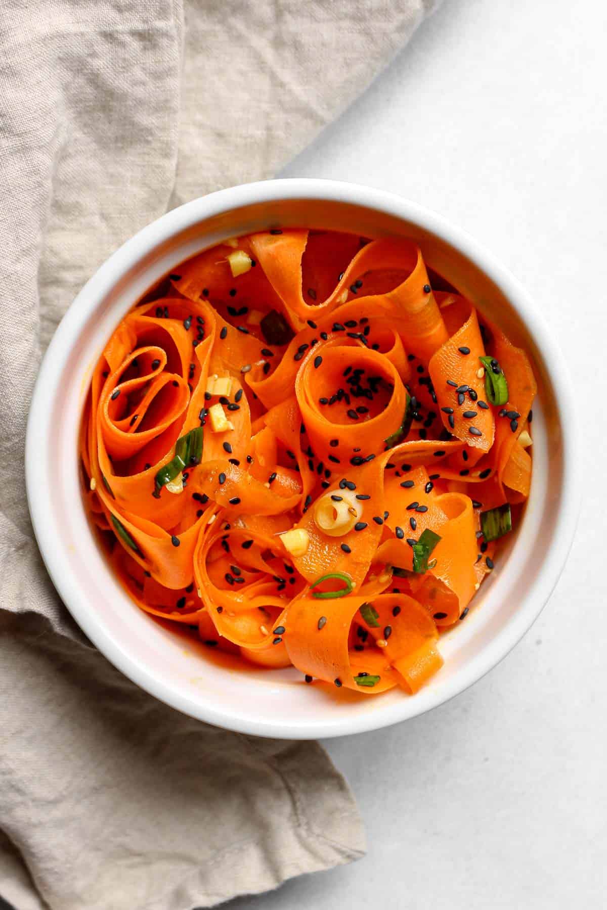 Sesame raw carrot salad served in a white bowl alongside a tan napkin