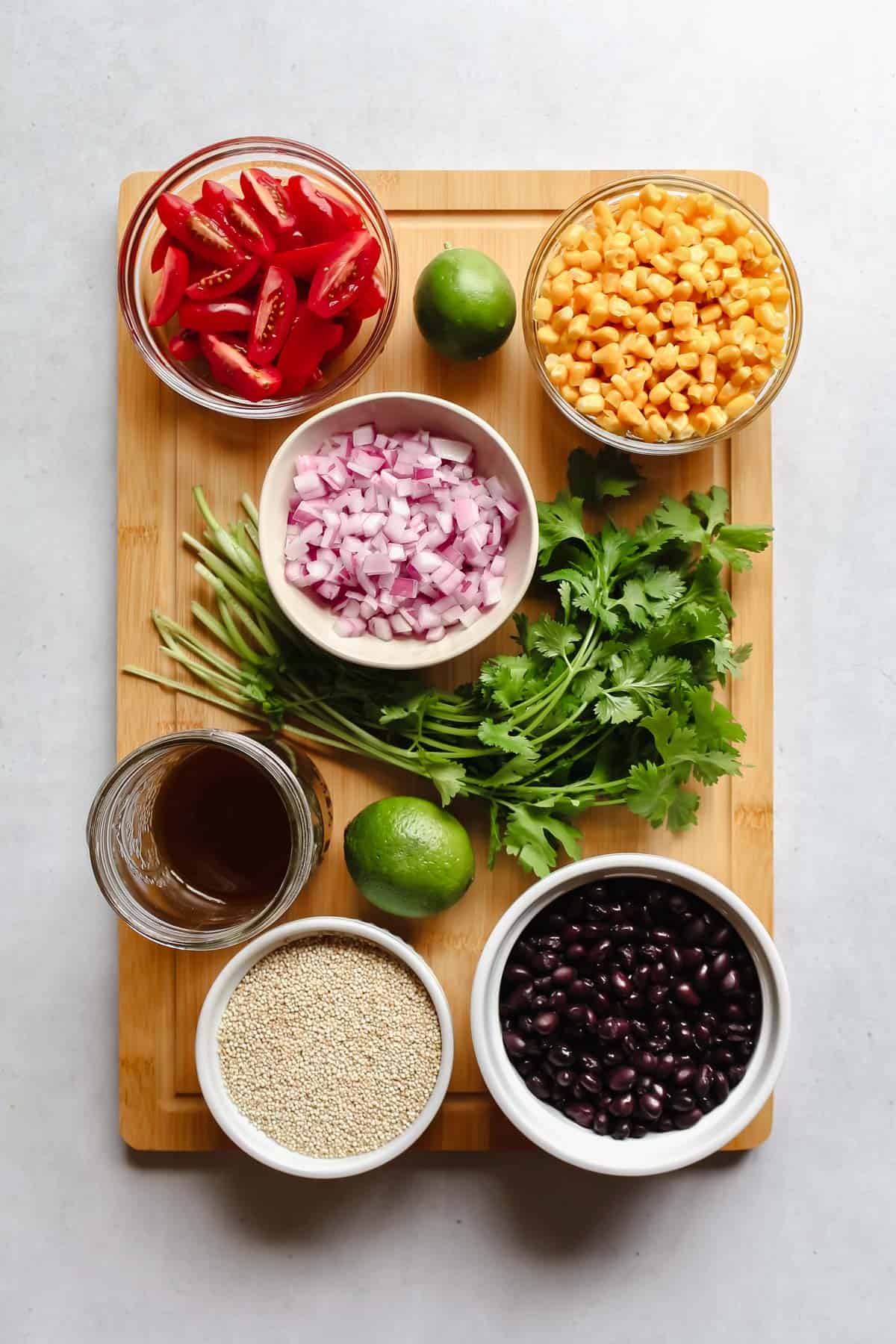 Recipe ingredients in individual bowls on a wooden cutting board on a white background
