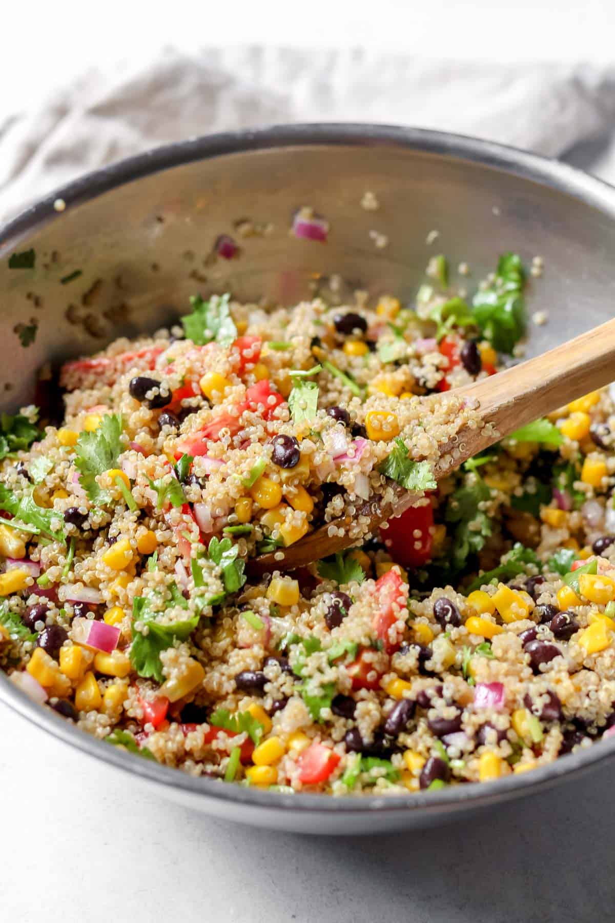 Tossing together the Black Bean, Corn, and Quinoa Salad ingredients with a wooden spoon in a stainless steel mixing bowl