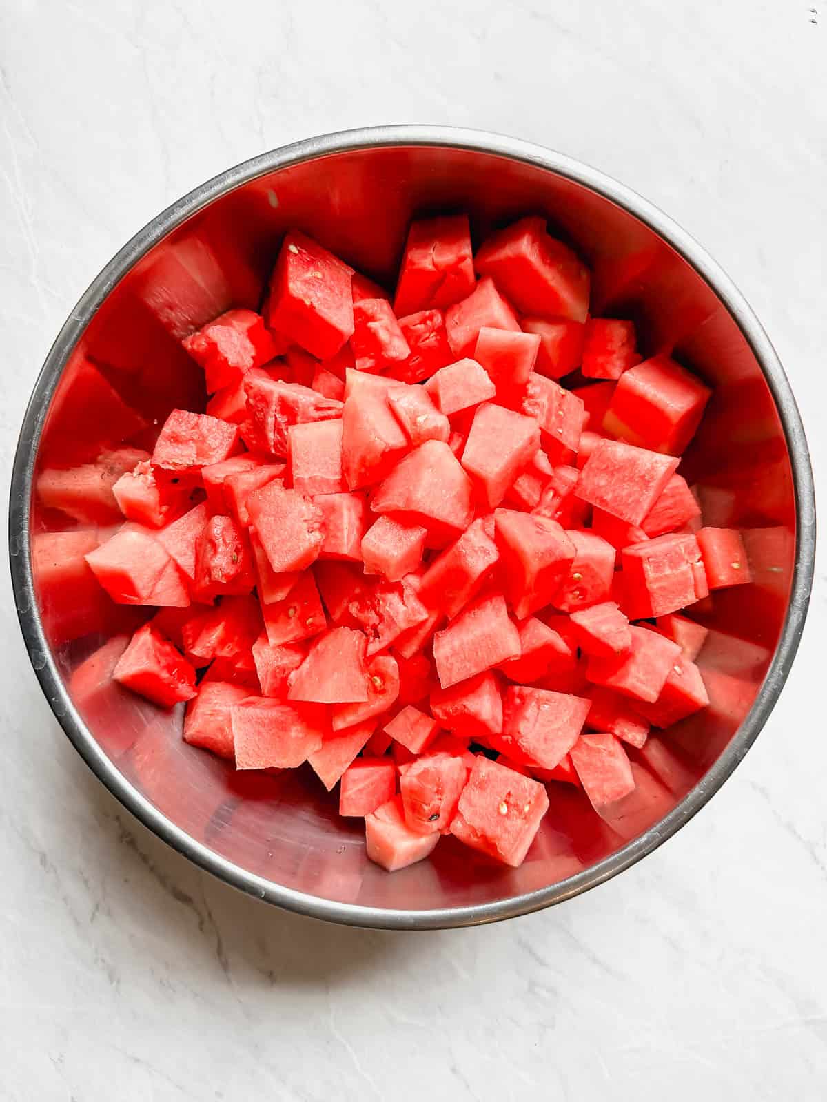 Cut up watermelon in a stainless steel mixing bowl