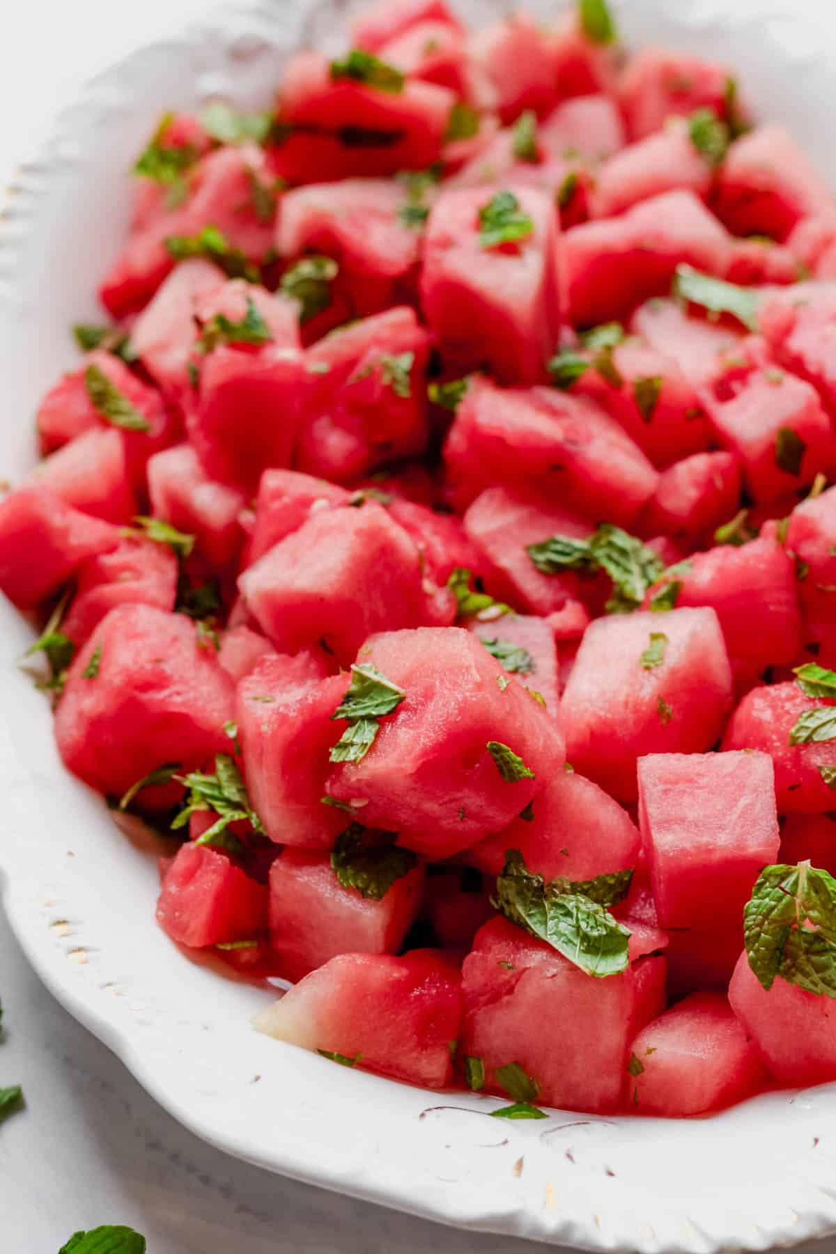 Cut up watermelon tossed with lime juice and mint in a white serving platter