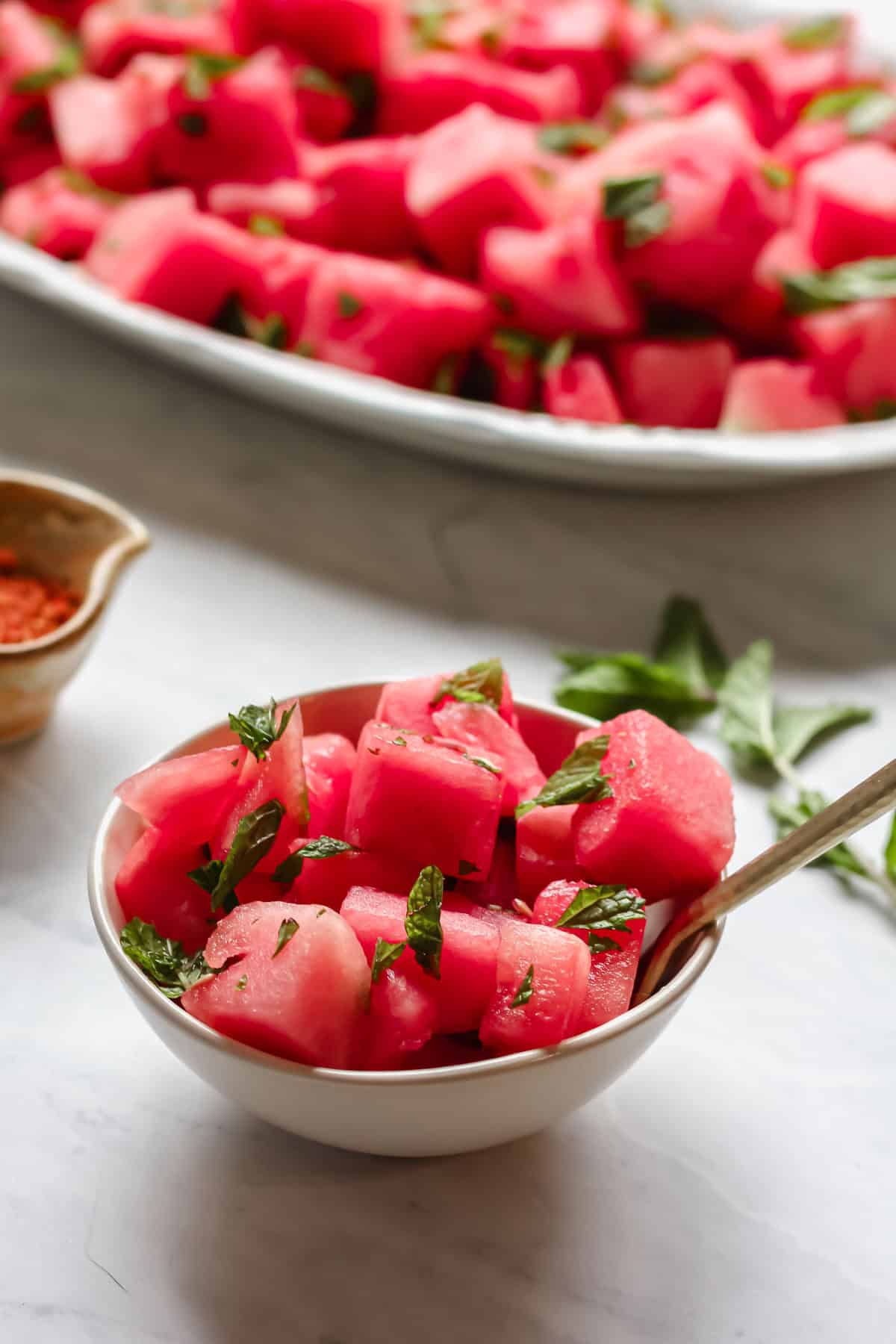 Cut up watermelon garnished with mint in a white bowl with a golden fork
